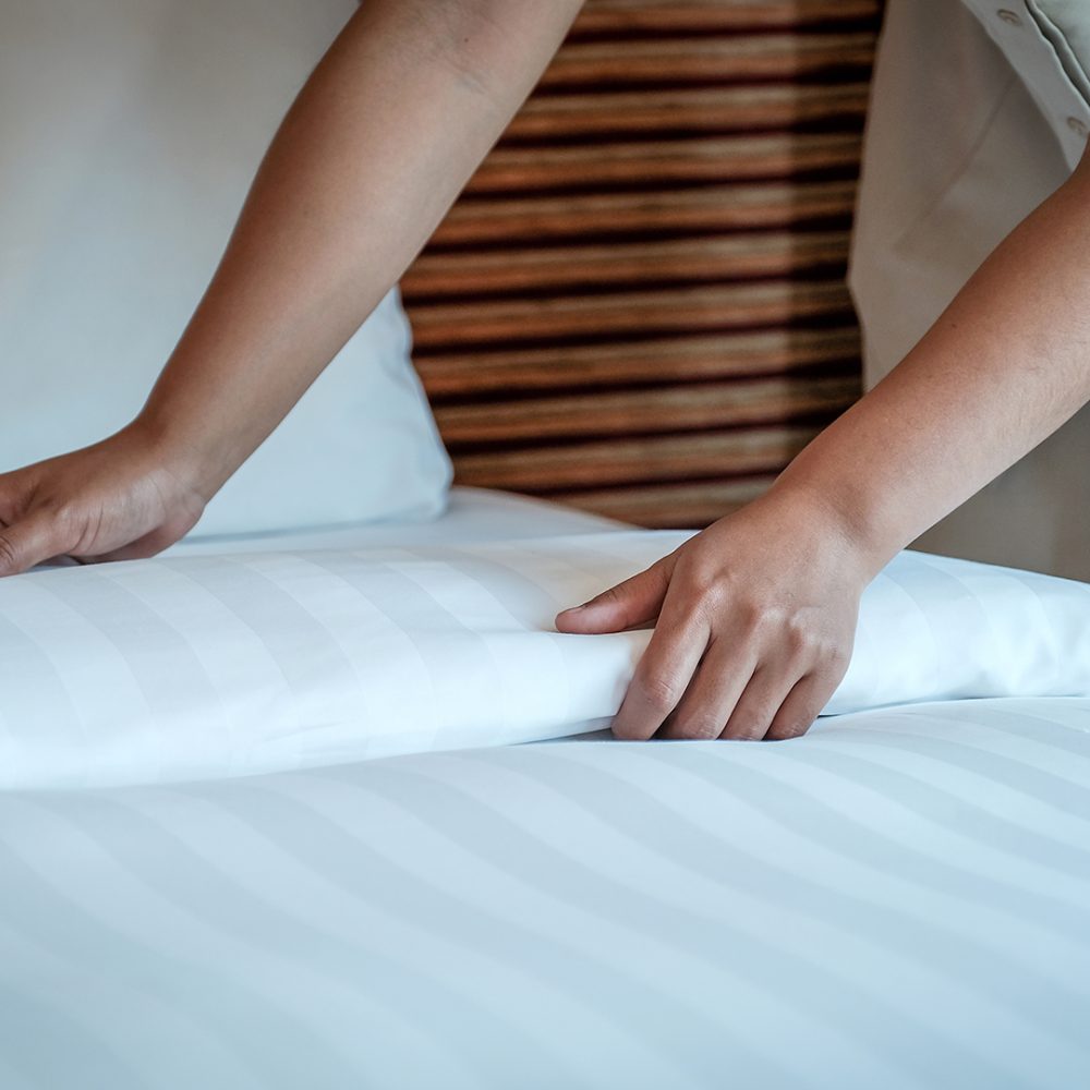 Hands of hotel maid making the bed in the luxury hotel room ready for tourist travel.